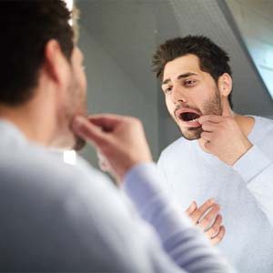 a person looking at their teeth in the mirror to inspect them for damage